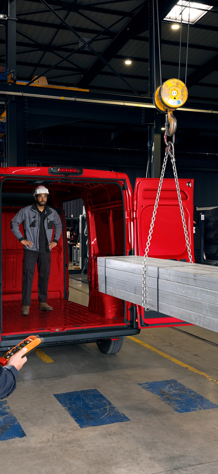 Rear view of a red Citroën Relay being loaded with metal beams in an industrial setting, highlighting large cargo volume and heavy-duty capability.