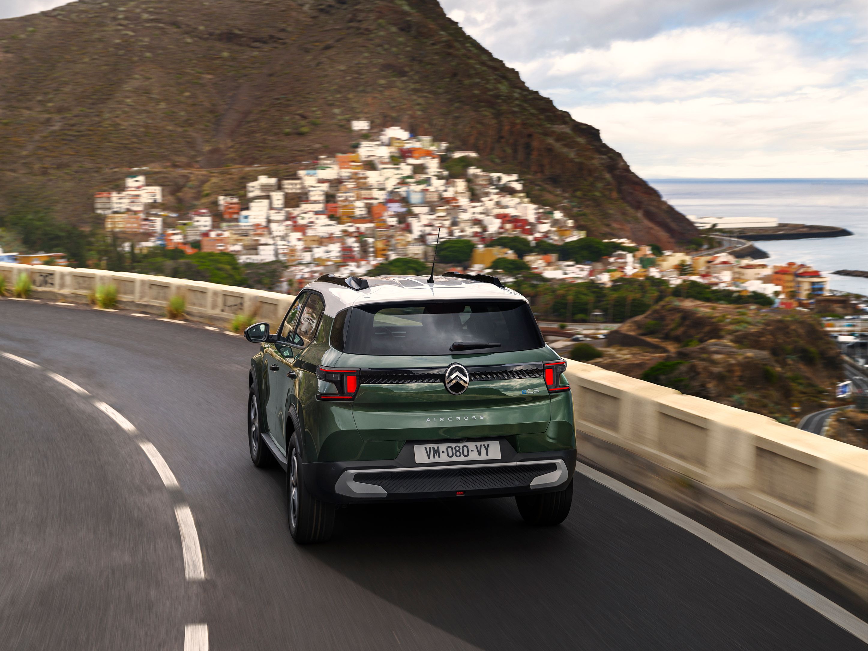 Rear three‑quarter driving view of Citroën C3 Aircross SUV on a coastal road for confident, smooth and affordable everyday mobility.